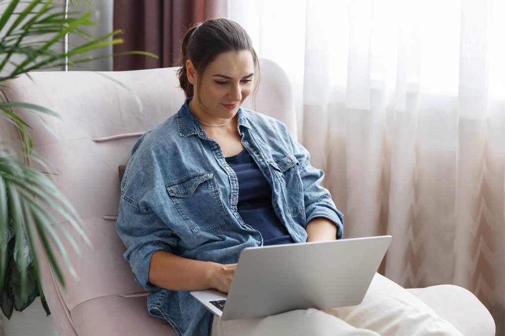 Afbeelding van een vrouw die op de bank met een laptop een website bezoekt.